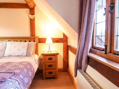 A bedroom with a wooden bed frame bedside table with lamp window with curtains and radiator at The Old House in Llanidloes