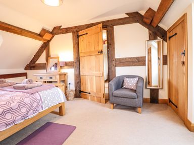 A bedroom with wooden bed and desk a grey chair a wall mirror and wooden beams at The Old House in Llanidloes