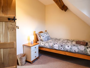 A bedroom with a single bed a bedside table with a lamp and a wicker wastebasket at The Old House in Llanidloes