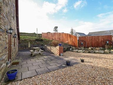An outdoor patio area with a wooden picnic table and potted plants next to a stone wall at The Old House in Llanidloes