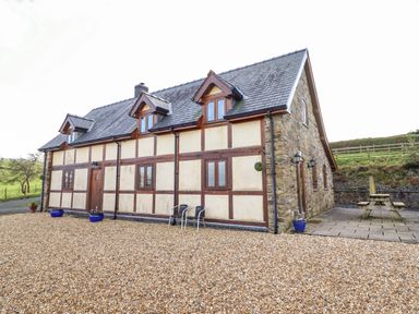 An exterior view of a two-story house with a gravel front yard and a stone patio with a picnic table at The Old House in Llanidloes