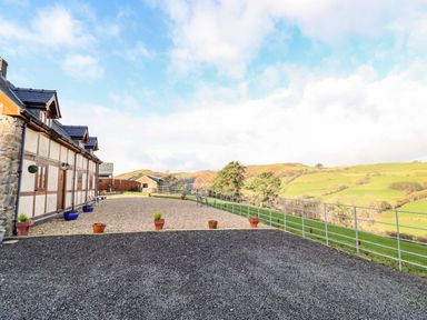 An outdoor area with gravel and potted plants next to a house with a stone and wood exterior and a metal fence overlooking green hills at The Old House in Llanidloes