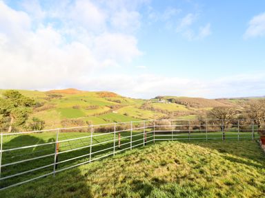 A grassy field with metal fencing and rolling hills in the background at The Old House in Llanidloes