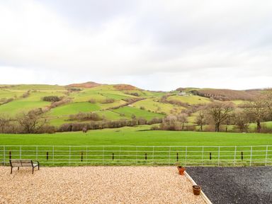 A landscape view of green fields and hills with a bench and gravel area at The Old House in Llanidloes
