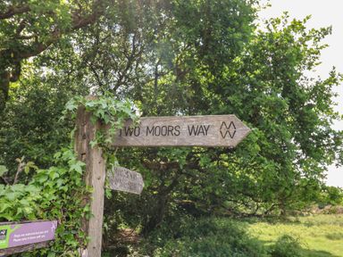 A wooden signpost for Two Moors Way in a wooded area at West Bowden Farm Knowstone near South Molton