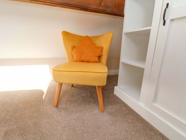 A reading nook with a yellow chair and cushion at Heather Croft in Robin Hood's Bay