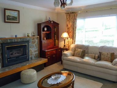 A living room with a stone fireplace a leather sofa cushions a wooden cabinet a lamp and a window with curtains at Eileen's in Aughavas near Mohill County Leitrim