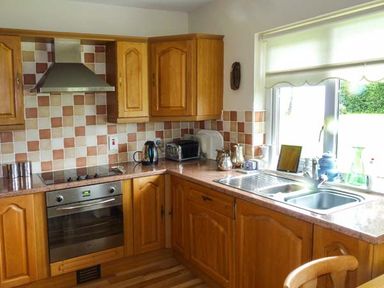 A kitchen with wooden cabinets a sink an oven a kettle a toaster and a window at Eileen's in Aughavas near Mohill County Leitrim