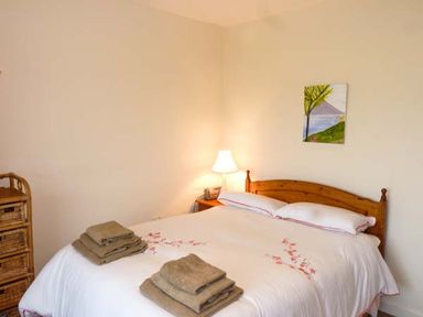 A bedroom with a double bed with folded towels a bedside table with a lamp a wicker drawer unit and a painting on the wall at Eileen's in Aughavas near Mohill County Leitrim