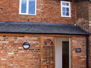 A brick exterior wall with a wooden door open and two windows above at Cotswold View in Clifford Chambers near Stratford-upon-Avon
