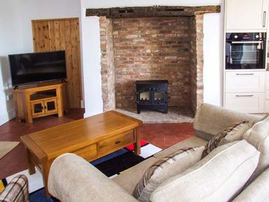 A living room with a beige sofa a wooden coffee table a TV on wooden stand a brick fireplace and a built-in oven at Cotswold View in Clifford Chambers near Stratford-upon-Avon