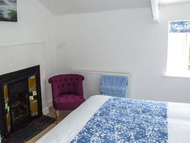 A bedroom with a bed covered in blue and white bedding a purple chair a fireplace and a window with blue floral blinds at Cotswold View in Clifford Chambers near Stratford-upon-Avon