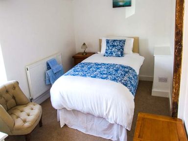 A bedroom with a single bed with blue patterned bedding a beige chair and wooden furniture at Cotswold View in Clifford Chambers near Stratford-upon-Avon