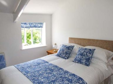 A bedroom with a bed with blue and white cushions and runner near a window with a blue patterned blind at Cotswold View in Clifford Chambers near Stratford-upon-Avon