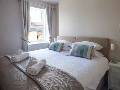 A bedroom with a double bed pillows rolled towels bedside lamp and window at Silversands Cottage Amble-by-the-Sea