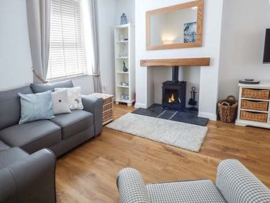 A living room with a gray sofa cushions a wood burning stove and shelving at Silversands Cottage in Amble-by-the-Sea
