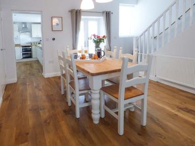 A dining room with a wooden table and six chairs near stairs and kitchen at Silversands Cottage in Amble-by-the-Sea