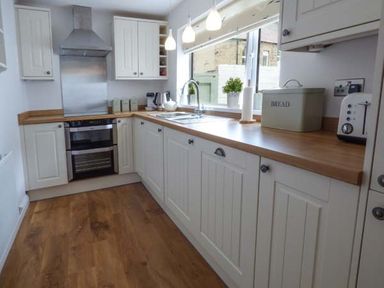 A kitchen with white cabinets wooden countertops a stove a sink a toaster and a bread box at Silversands Cottage in Amble-by-the-Sea