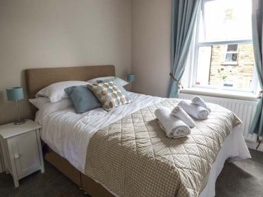 A bedroom with a double bed pillows folded towels on bed and window with curtains at Silversands Cottage in Amble-by-the-Sea