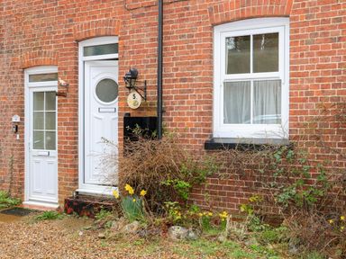 The entrance of a brick house with white doors and windows and plants in front at 5 Melinda Cottages in East Runton near Cromer