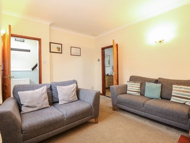 A living room with two grey sofas and cushions and doors leading to other rooms at 5 Melinda Cottages in East Runton near Cromer