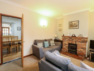 A living room with two grey sofas a brick fireplace and a wooden dining table visible through an open door at 5 Melinda Cottages in East Runton near Cromer