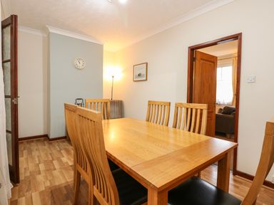 A dining room with a wooden table and chairs a wall clock a floor lamp and a doorway leading to a living room at 5 Melinda Cottages in East Runton near Cromer