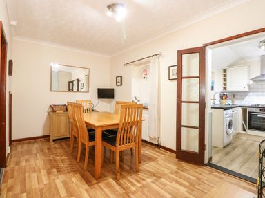 A dining room with a wooden table and chairs next to an open doorway to a kitchen at 5 Melinda Cottages in East Runton near Cromer