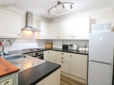A kitchen with white cabinets a refrigerator a microwave a toaster a kettle a gas stove and a sink at 5 Melinda Cottages in East Runton near Cromer