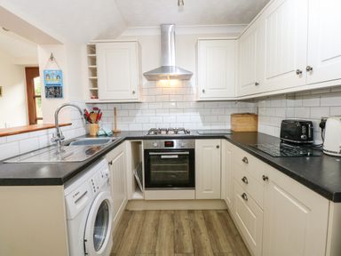 A kitchen with white cabinets black countertops a washing machine oven stove toaster and kettle at 5 Melinda Cottages East Runton near Cromer