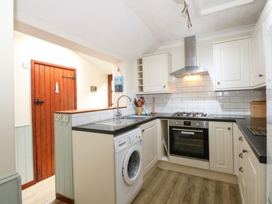 A kitchen with white cabinets a washing machine an oven a stove and a wooden door at 5 Melinda Cottages East Runton near Cromer