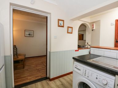 A kitchen area with a washing machine counter and an open doorway leading to a room with a chair and framed picture at 5 Melinda Cottages East Runton near Cromer
