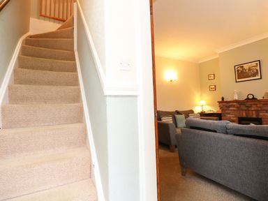 A carpeted staircase next to a living room with gray sofas and a brick fireplace at 5 Melinda Cottages in East Runton near Cromer