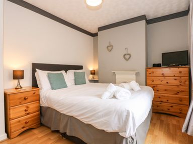 A bedroom with a double bed nightstands with lamps wooden dresser and a small television at 5 Melinda Cottages East Runton near Cromer