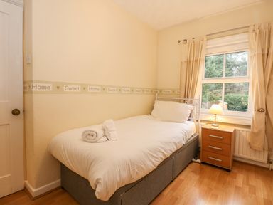 A small bedroom with a single bed a nightstand with a lamp and a window with curtains at 5 Melinda Cottages in East Runton near Cromer