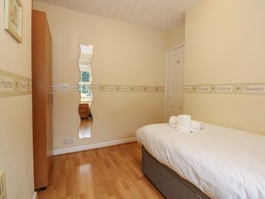 A bedroom with a single bed a wooden wardrobe a wavy wall mirror and a door at 5 Melinda Cottages East Runton near Cromer
