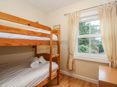A bedroom with wooden bunk beds next to a window and a small chest of drawers at 5 Melinda Cottages in East Runton near Cromer