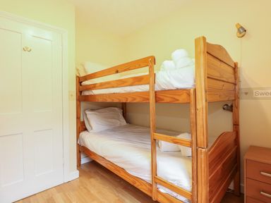 A bedroom with a wooden bunk bed white bedding a wooden nightstand and a closed door at 5 Melinda Cottages East Runton near Cromer