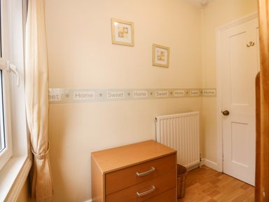 A small room with a wooden chest of drawers radiator and window with curtain at 5 Melinda Cottages East Runton near Cromer