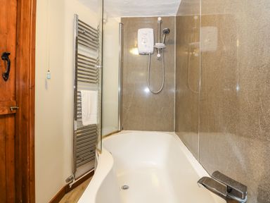 A bathtub with shower unit and glass screen in a bathroom at 5 Melinda Cottages East Runton near Cromer