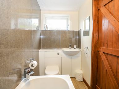 A bathroom with a bathtub a toilet a sink a mirror a wooden door and a window at 5 Melinda Cottages in East Runton near Cromer