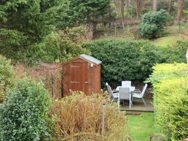 A garden area with a wooden shed and outdoor table with four chairs at 5 Melinda Cottages in East Runton near Cromer