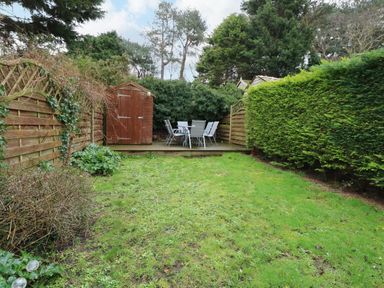 A garden with a grassy lawn a wooden shed and outdoor table with chairs at 5 Melinda Cottages in East Runton near Cromer