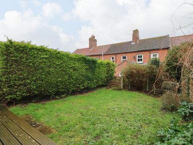A backyard garden with grass a wooden bench and hedge at 5 Melinda Cottages in East Runton near Cromer