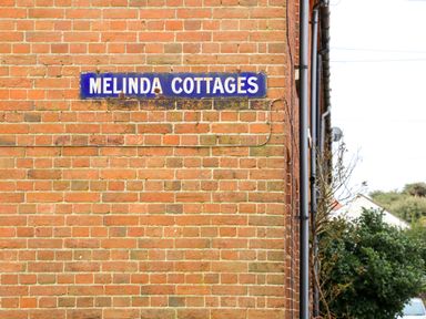 A brick wall with a blue sign reading Melinda Cottages at 5 Melinda Cottages in East Runton near Cromer
