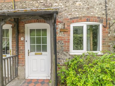An exterior view of a cottage entrance with a white door and window surrounded by brick and stone walls at Apple Tree Cottage in Shillingstone near Sturminster Newton