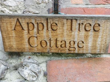 A wooden sign reading Apple Tree Cottage mounted on a brick and stone wall at Apple Tree Cottage in Shillingstone near Sturminster Newton