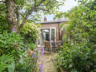 A garden with a patio table and chairs surrounded by plants and flowers at Apple Tree Cottage in Shillingstone near Sturminster Newton
