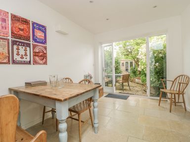 A dining area with wooden table and chairs next to glass doors opening to a garden patio at Apple Tree Cottage in Shillingstone near Sturminster Newton