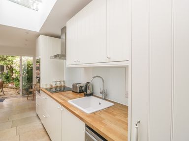 A kitchen with white cabinets wooden countertop a sink toaster kettle and a view of the garden at Apple Tree Cottage in Shillingstone near Sturminster Newton